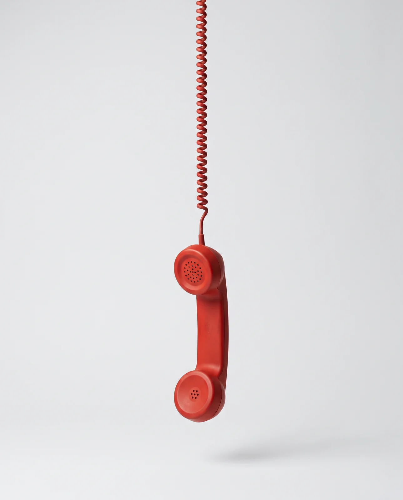 Red telephone handset hanging from its cord on a grey studio backdrop